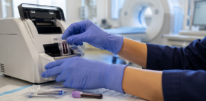 Gloved hands load blood samples into a laboratory analyzer in a clinical testing room