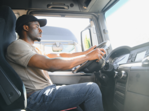Focused truck driver wearing a cap, gripping the wheel while driving a commercial vehicle