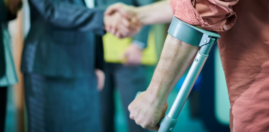 Person using crutch in foreground while two professionals shake hands, symbolizing injury settlement agreement