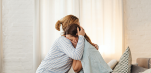 Woman comforting upset girl with a hug on couch, showing emotional support after distress or trauma