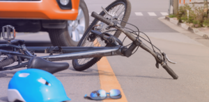 Bicycle lying on the roadway near a vehicle with a helmet and sunglasses on the ground, suggesting a bicycle accident scene