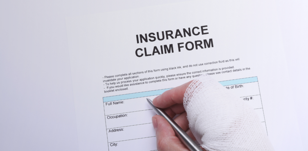 Person with a bandaged hand filling out an insurance claim form with a pen