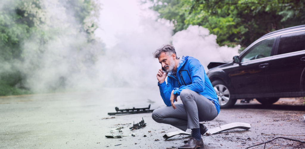 Driver crouches near a smoking car while talking on a phone after a roadside incident