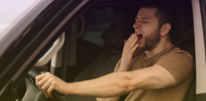 Driver yawns while holding the steering wheel, showing signs of fatigue