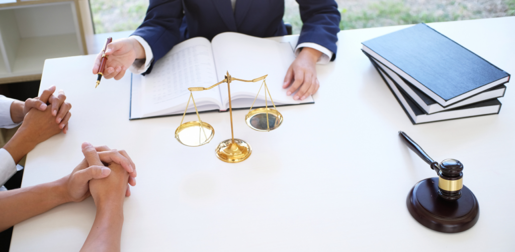 Legal professional meeting with clients at a desk featuring scales of justice, a gavel, and open reference materials