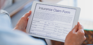 Person holding a tablet displaying a digital insurance claim form, reviewing personal information fields and application details for submission