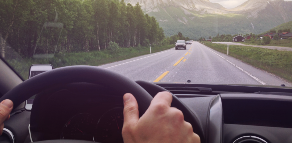 View from behind the steering wheel on a highway with mountains and oncoming traffic