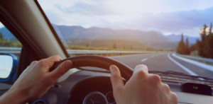 Driver holds the steering wheel while traveling along a curving highway toward distant mountains