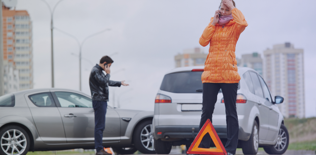 Two drivers make phone calls after a traffic collision, with a warning triangle behind their vehicles
