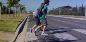Two children wearing backpacks walk across a marked pedestrian crosswalk on a sunny day